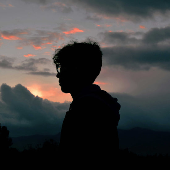 Silhouette of a person against a dramatic sunset sky with clouds.