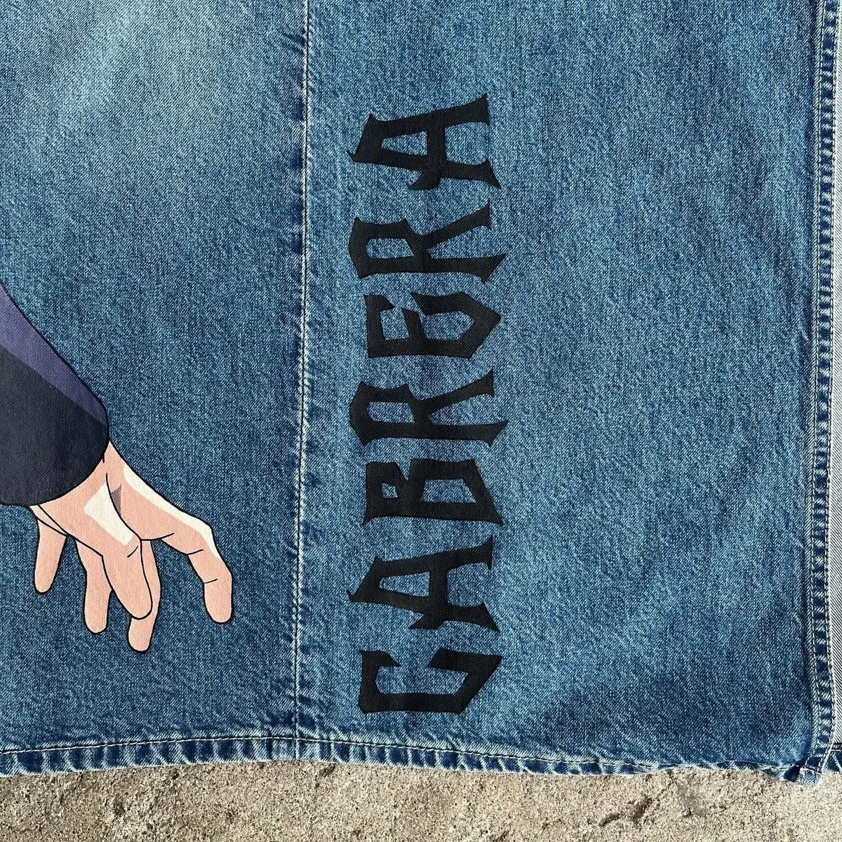 Close-up of Y2K Anime Baggy Jeans featuring hand illustration and bold "CABRERA" text on denim fabric.
