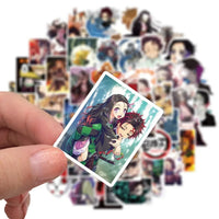 A mixed pack of waterproof Demon Slayer Stickers featuring cute Tanjiro and Nezuko anime art, applied to a laptop and phone case.